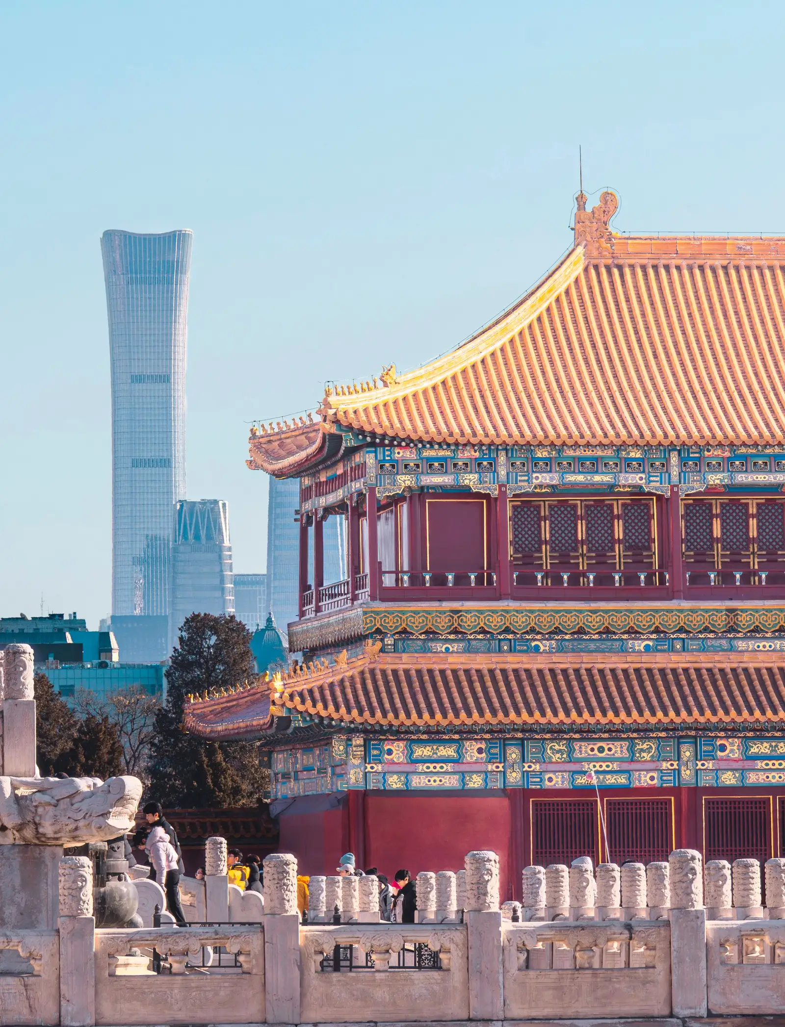 Red walls and yellow roofs of a Forbidden City hall with a modern tower beyond