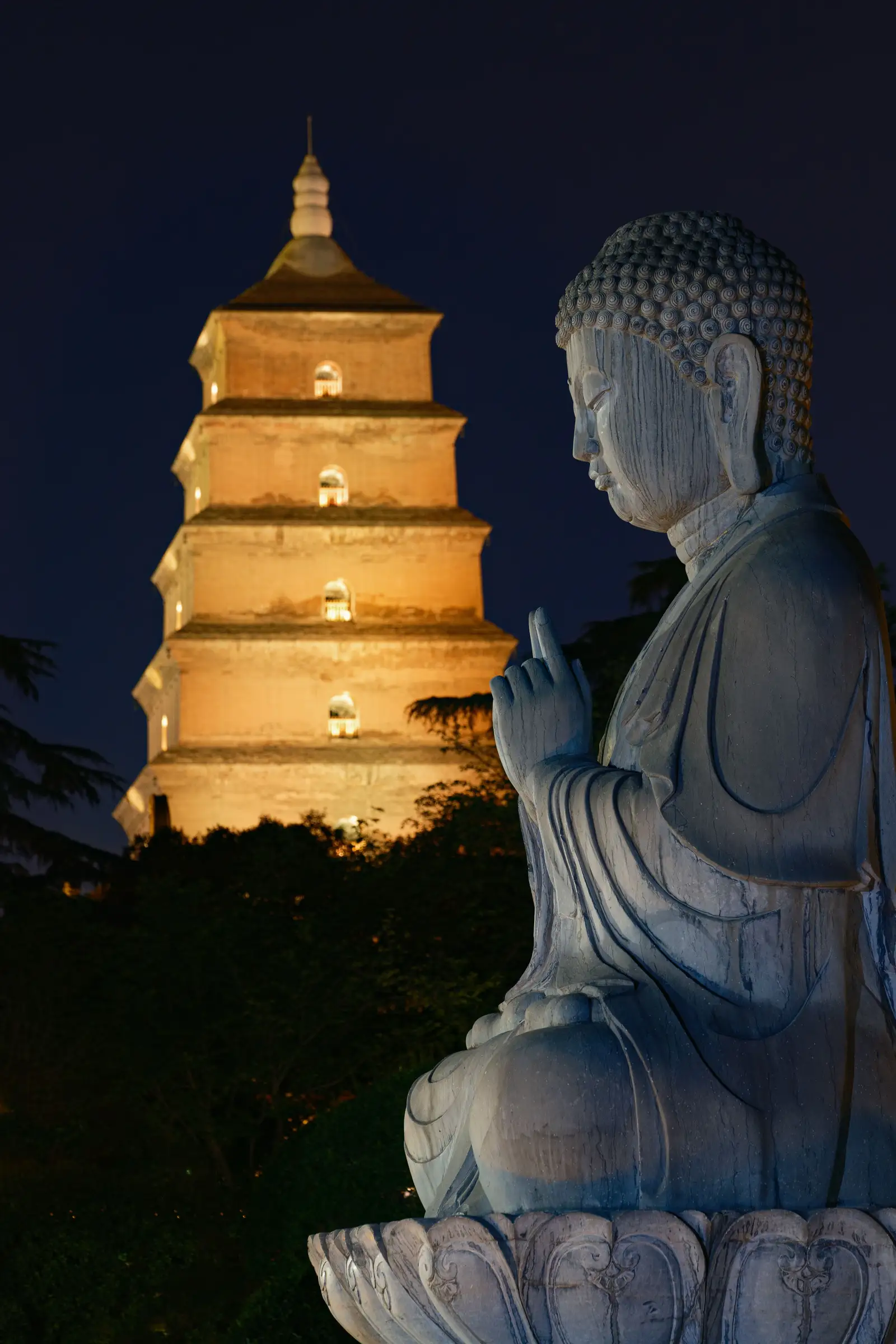 The Big Wild Goose Pagoda lit at night beside a stone Buddha